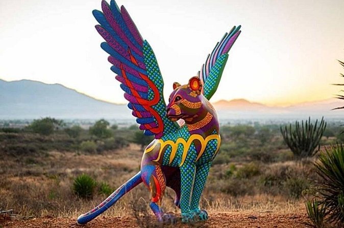 A carved and painted alebrije standing in the open with the valley behind it